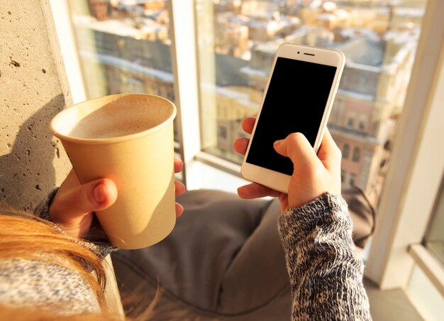 Handen met kopje koffie en smartphone