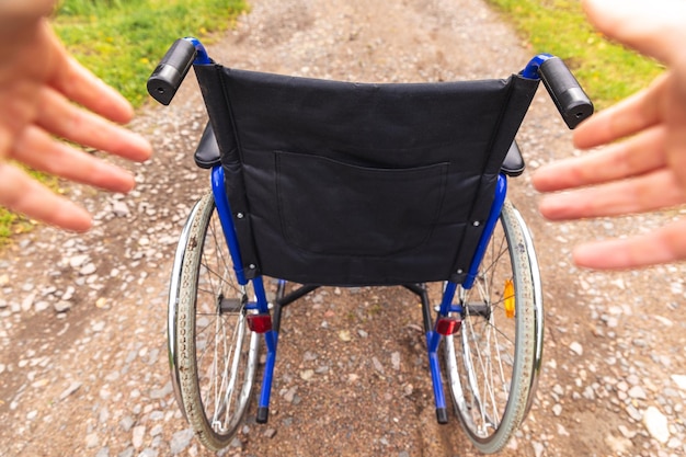Handen met lege rolstoel in ziekenhuispark wachtend op patiëntendiensten rolstoel voor persoon...