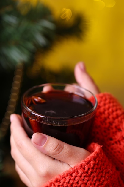 Handen met mok warme drank, close-up, op kerstboom achtergrond