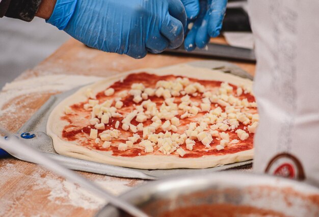 Handen met plastic handschoenen die verse mozzarella toevoegen aan een pizza met tomatensaus op een houten plank