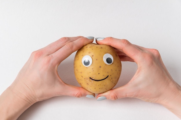 Handen met rauwe aardappelen met Googly eyes en glimlach Groenten met grappig gezicht