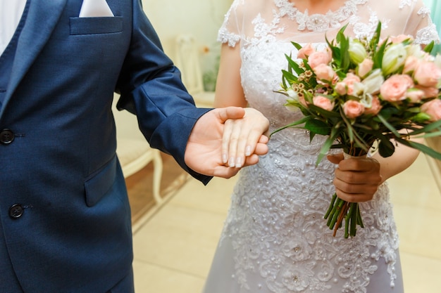 Handen met ringen. De bruidegom begeleidt de bruid naar de huwelijksceremonie.