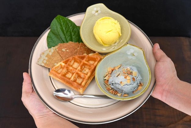 Handen met schotel met biologisch ijs en Belgische wafels op houten tafel achtergrond