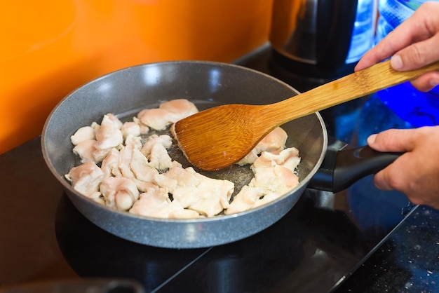 Handen met spatel roergebakken kip in een koekenpan voor het bereiden van japanse ramen