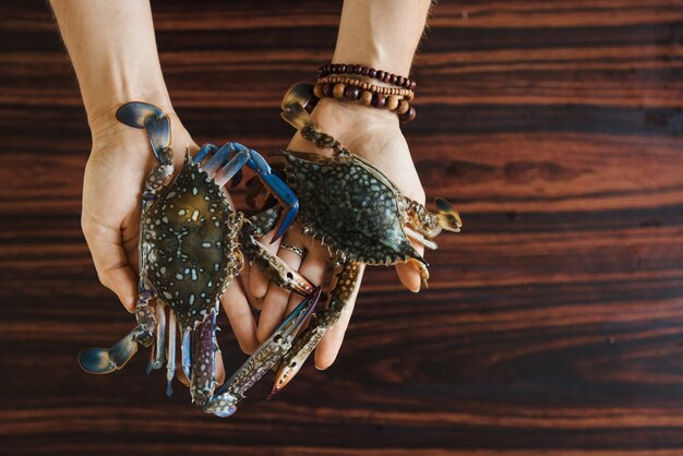Handen met twee kleurrijke verse krabben op houten tafel achtergrond voor het koken. bovenaanzicht met kopieerruimte