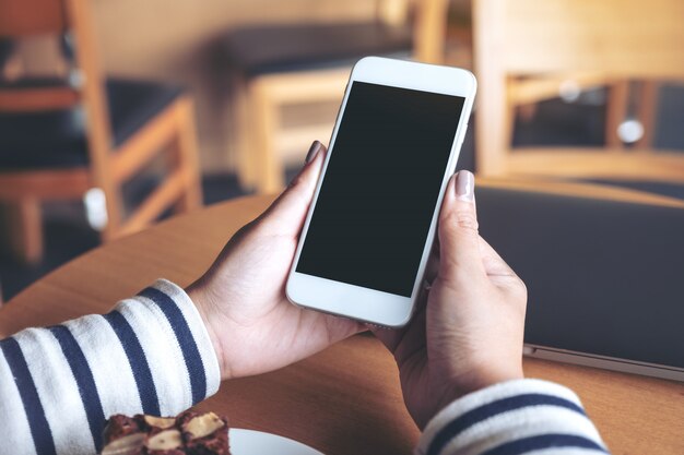 handen met witte mobiele telefoon met leeg scherm in houten café