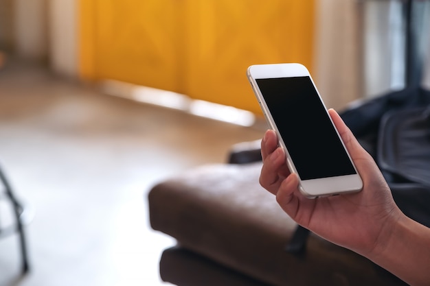 Handen met witte mobiele telefoon met leeg zwart scherm in café