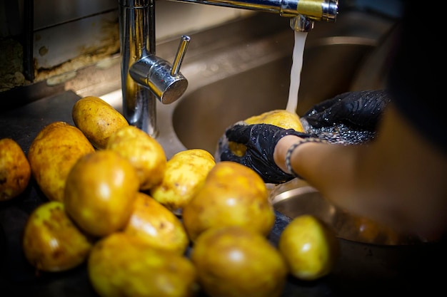 Handen met zwarte plastic handschoenen die aardappelen wassen onder de kraan