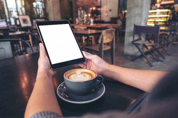 Handen met zwarte tablet-pc met een leeg wit scherm met koffiekopje