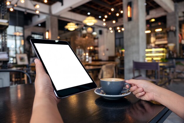 Handen met zwarte tablet-pc met een leeg wit scherm tijdens het drinken van koffie