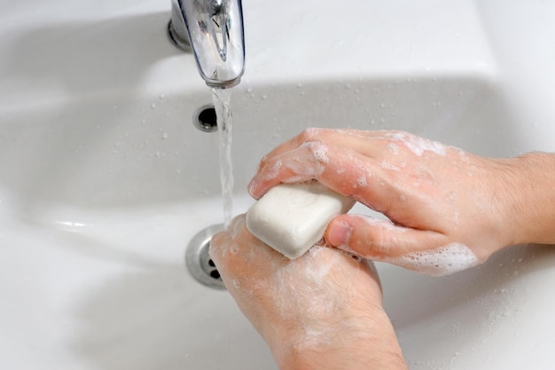 Handen onder de kraan met water boven de gootsteen in de badkamer Hygiëneconcept