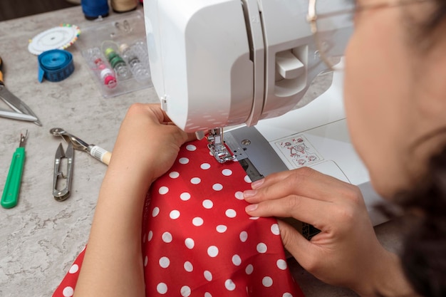 Handen op aantrekkelijke Latijns-vrouw met behulp van naaimachine plus schaar draden stof maken van kleding