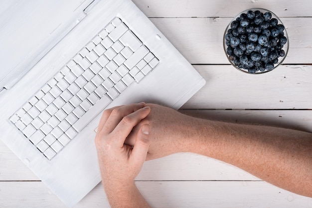 Handen op de computer en bosbessen op een houten witte tafel gezonde snack concept