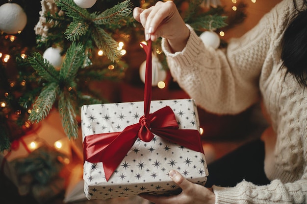 Handen openen kerstcadeau met rode strik tegen kerstboom met lampjes Merry Christmas