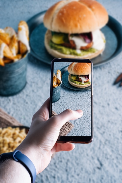 Handen oppakken van een smartphone met een foto van een hamburger. Ruimte voor tekst. Selectieve aandacht