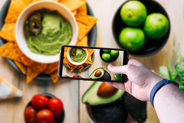 Handen oppakken van een smartphone met een foto van een kom met guacamole. Ruimte voor tekst. Selectieve aandacht