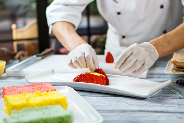 Handen raken plakjes aardbei. Bord met stukjes bes. Vlaai met verse aardbeien. Banketbakker aan het werk.