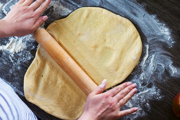 Handen rollingpin en deeg voor brood pasta of pizza op houten tafel