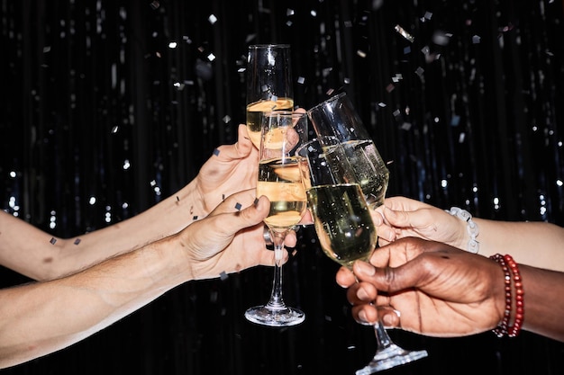 Foto handen roosteren met champagneglazen op feestje met confetti