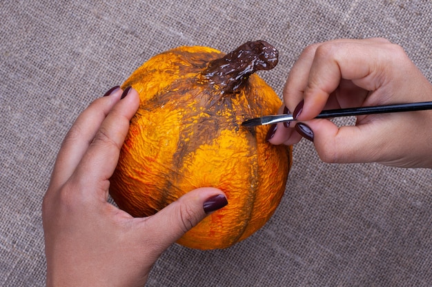 handen schilderen met een penseel met gouache oranje kleuren ambachtelijke pompoen van papier-maché voor Halloween