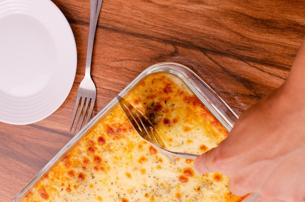 Handen snijden lasagne op glazen schotel Koken concept samenstelling van het koken van lasagne op houten.