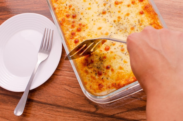Handen snijden lasagne op glazen schotel Koken concept samenstelling van het koken van lasagne op houten.