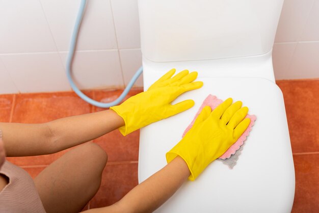 Handen van Aziatische vrouw die de wc-bril schoonmaakt met een roze doek die het toilet in huis afveegt