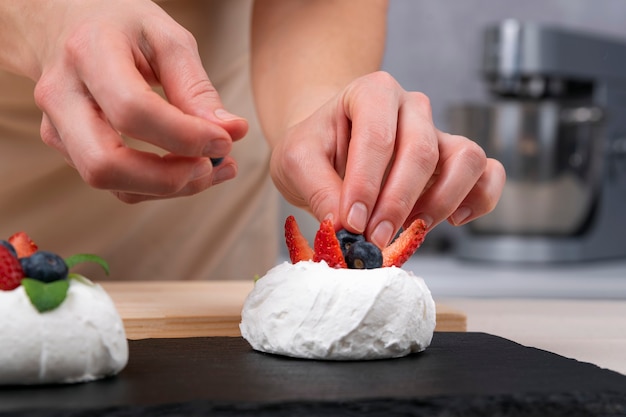 Handen van banketbakker versiert cake met verse aardbeien en bosbessen