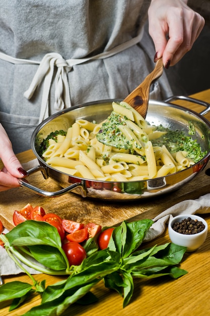 Handen van chef-kok die Penne-deegwaren met spinazie voorbereidt.