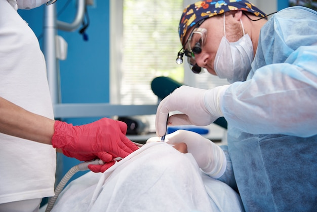 Handen van de chirurg van de tandarts en de assistent met het instrument tijdens de operatie.