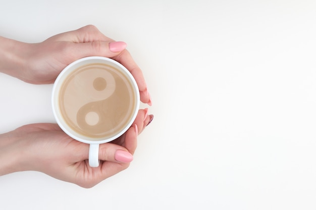 Handen van de kop van de vrouwenholding van latte met Yin en Yang-beeld op het, exemplaarruimte