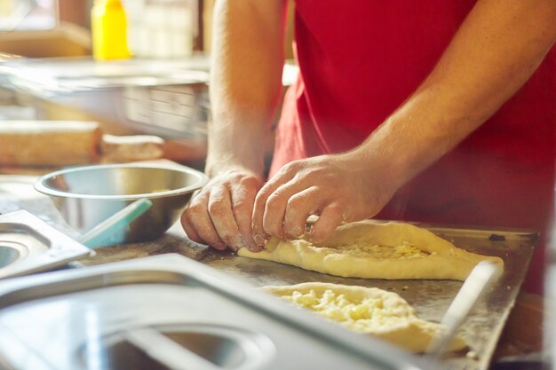 Handen van de mens die khachapuri, op de het deegkaas van de lijstbloem voorbereiden