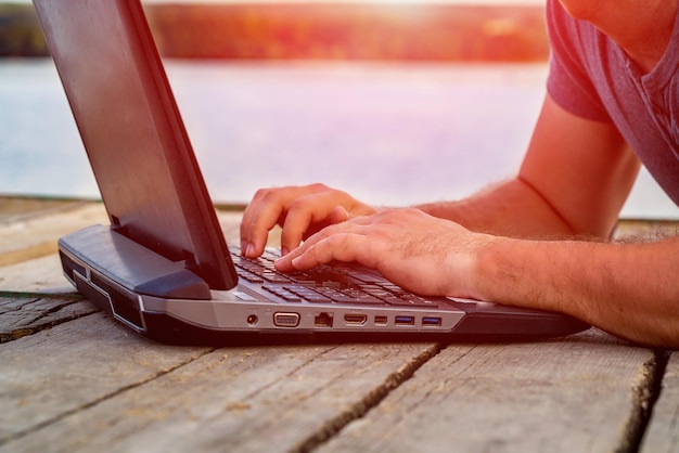 Foto handen van de mens typen tekst op een laptop in de zomer op de achtergrond van de rivier