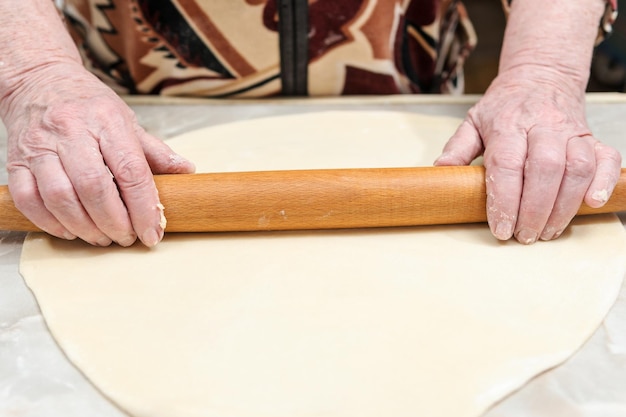 Handen van de oude vrouw rollen het deeg op tafel