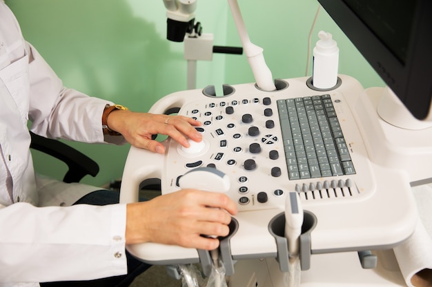 Handen van een arts in een witte jas besturen de ultrasone machine