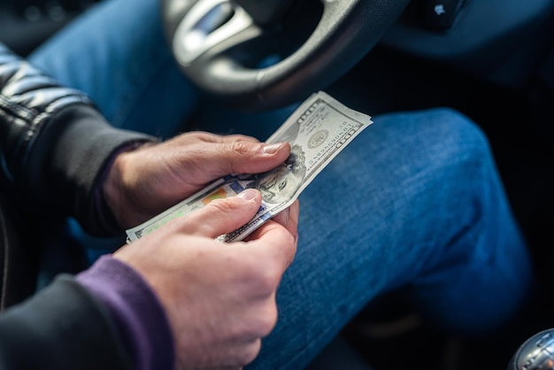 Handen van een autobestuurder met bankbiljetten van dollars in het midden in de auto. Bedrijfsconcept. Het concept van het kopen van een auto