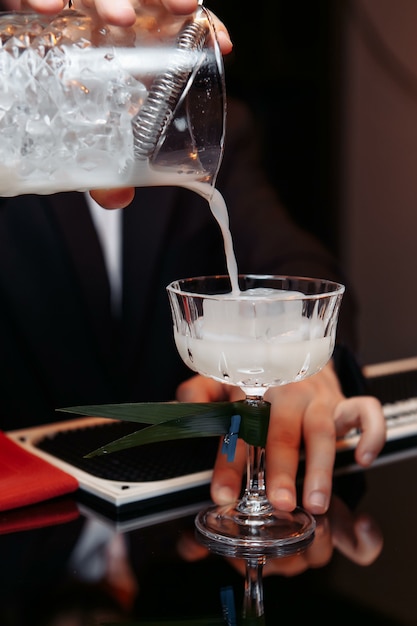 Handen van een barman die een shaker houdt die een drankje in een glas giet.