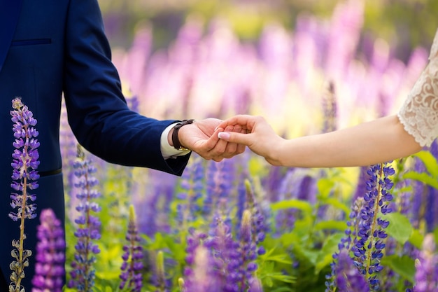 Handen van een bruid en bruidegom in trouwdag op de achtergrond van lavendelveld Jong verliefd koppel geniet van het moment van geluk in de zomer onder paarse bloemen