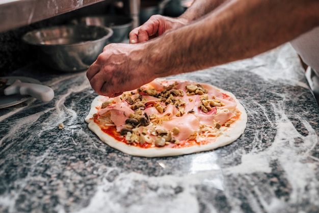 Handen van een chef-kok die pizza voorbereidt.