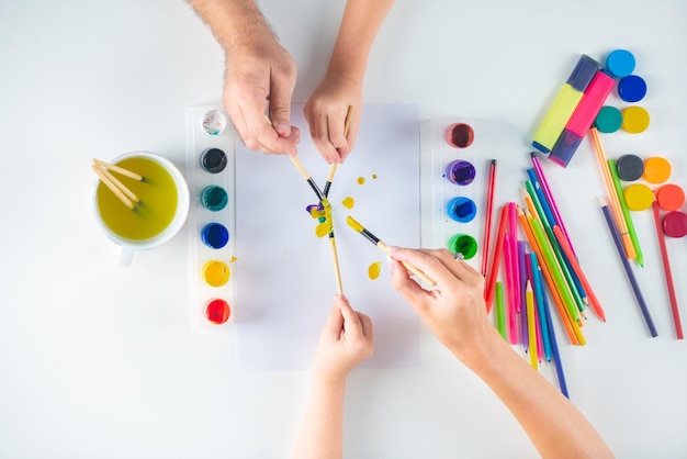 Handen van een familietekening met potlood en verven bovenaanzicht naar witte tafel met kunstbenodigdheden artiest pa