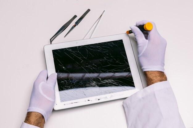 Handen van een gehandschoende technicus die een tablet met een gebroken glas herstelt