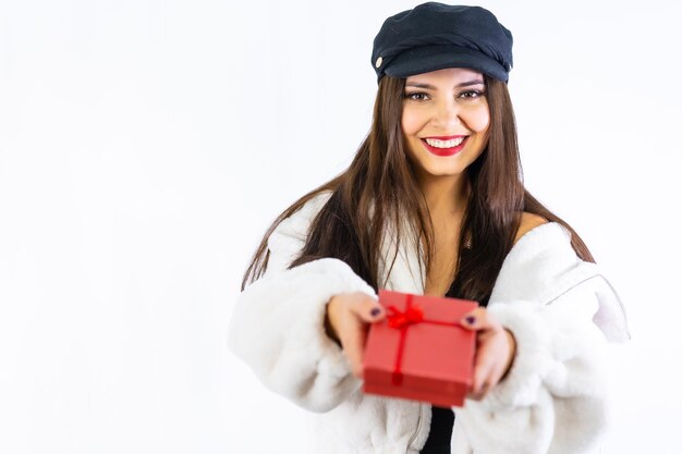 Handen van een jong Latijns brunette meisje dat vreugdevol een geschenk op een witte achtergrond overhandigt. Portret naar het model met een rode geschenkdoos