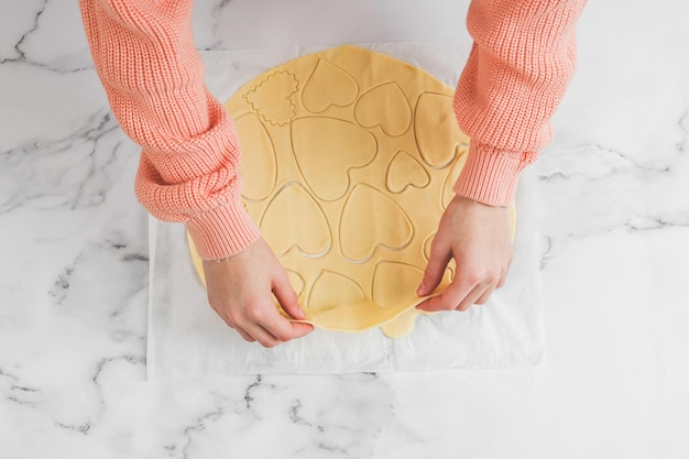 Handen van een jonge blanke meisjesbakker tijdens het scheiden van het rauwe deeg met hartuitsparingen