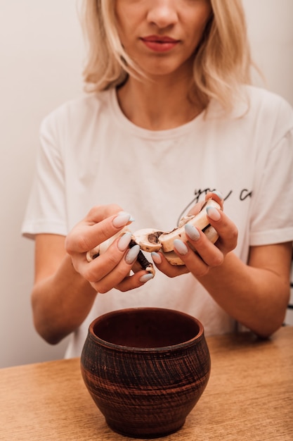 Handen van een jonge vrouw die gehakte champignons in een bakpot in de keuken giet