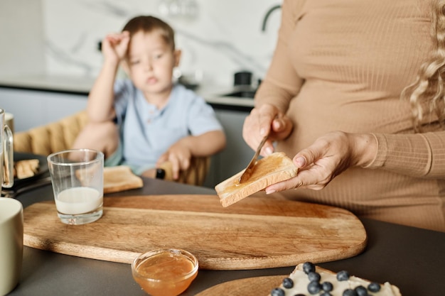 Handen van een jonge zwangere vrouw die honing of jam op een sneetje tarwebrood verspreidt