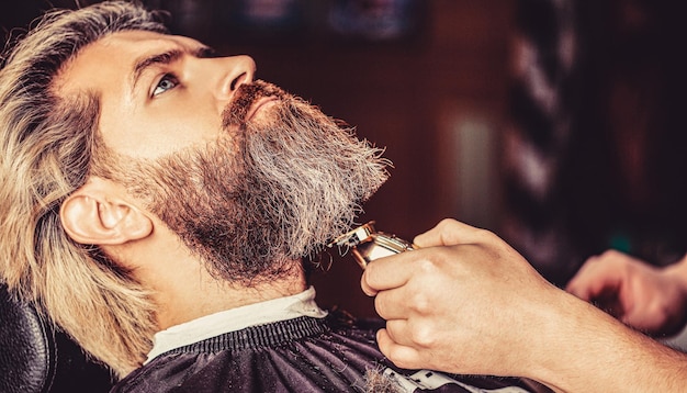 Handen van een kapper met een baardknipper close-up Bebaarde man in kapperszaak Man op bezoek bij haarstylist in kapperszaak