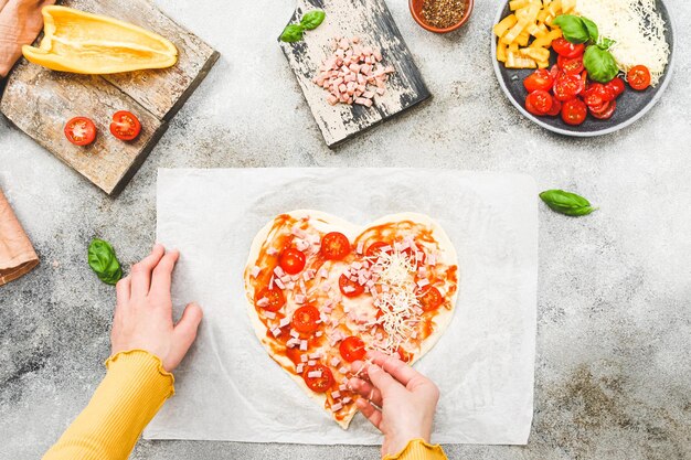 Handen van een kaukasisch tienermeisje leggen gesneden cherrytomaat op hartvormig pizzadeeg