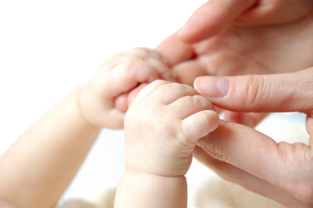 Handen van een kleine pasgeboren baby houden zich vast aan de vingers van haar moeders handen op een wit