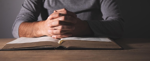 Handen van een man die bidt over een Bijbel