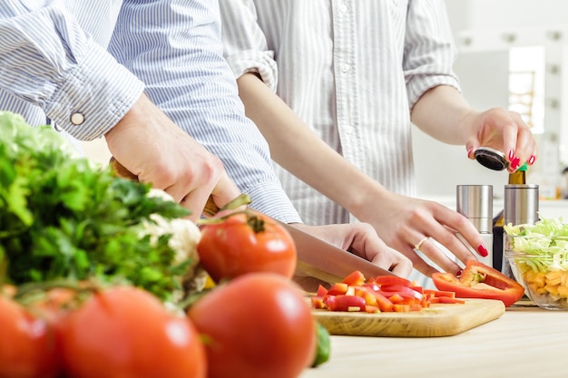 Handen van een man gehakte rode paprika voor salade op een bord. Paar hakken van groenten in de keuken